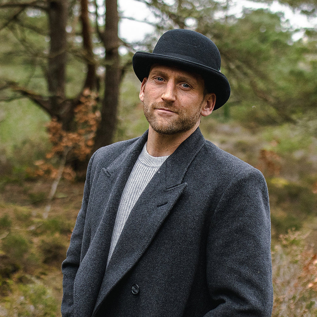 Black bowler hat with curved brim, grosgrain band and feather detail