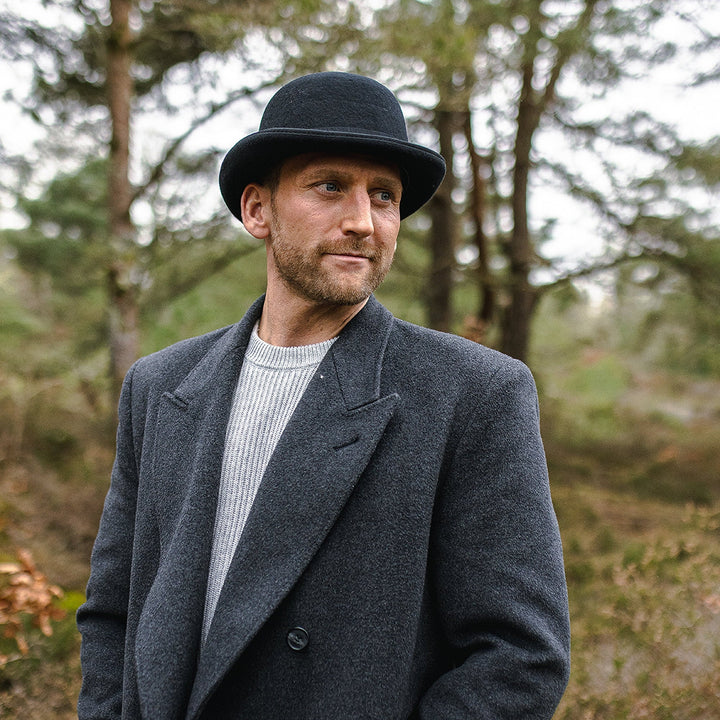 Black bowler hat with curved brim, grosgrain band and feather detail