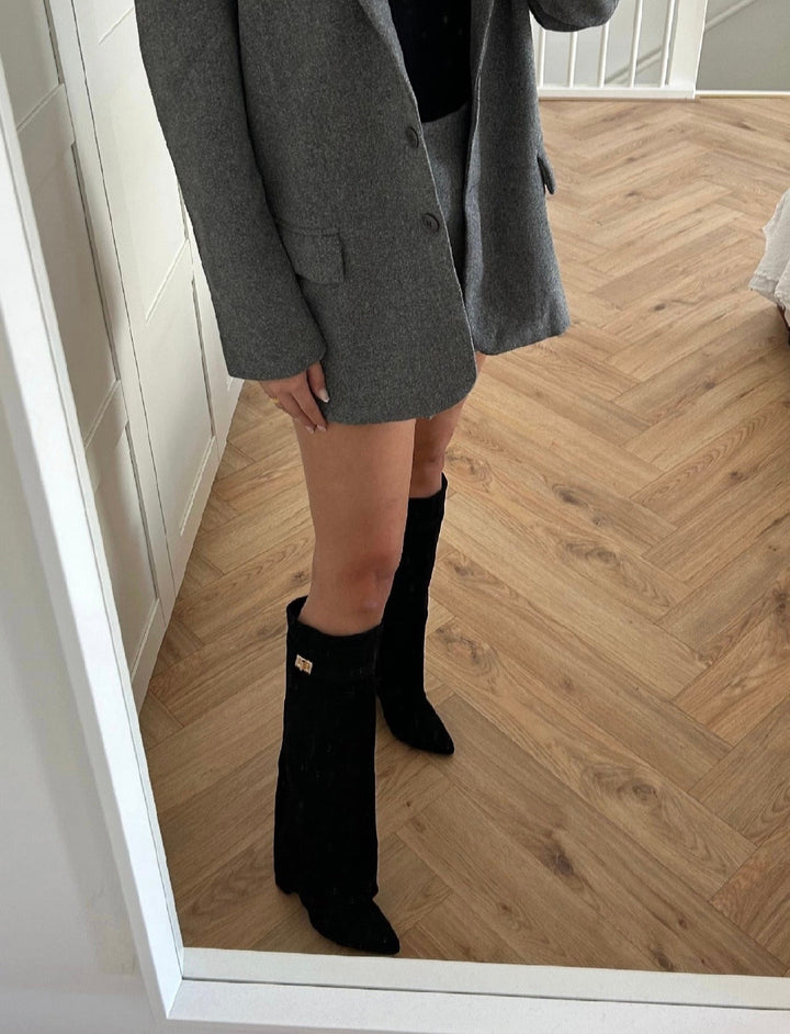 Black knee-high boots with pointed toes, low heels and decorative buckle trim