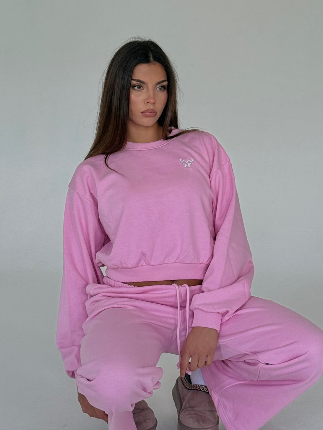 Women's pink cropped crewneck sweatshirt with long sleeves and white chest logo
