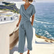 Women's wrap top and cropped trousers set in neutral tone, styled on a terrace overlooking the ocean